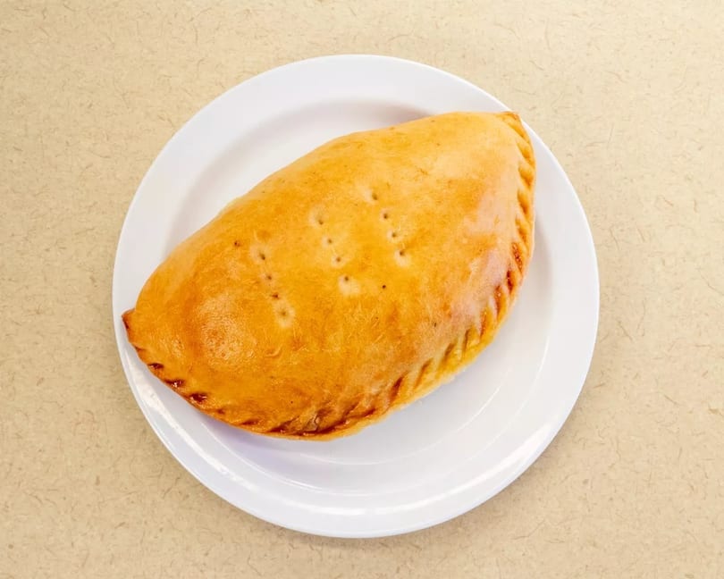Golden brown calzone with crimped edges and small vents, served on a white plate.
